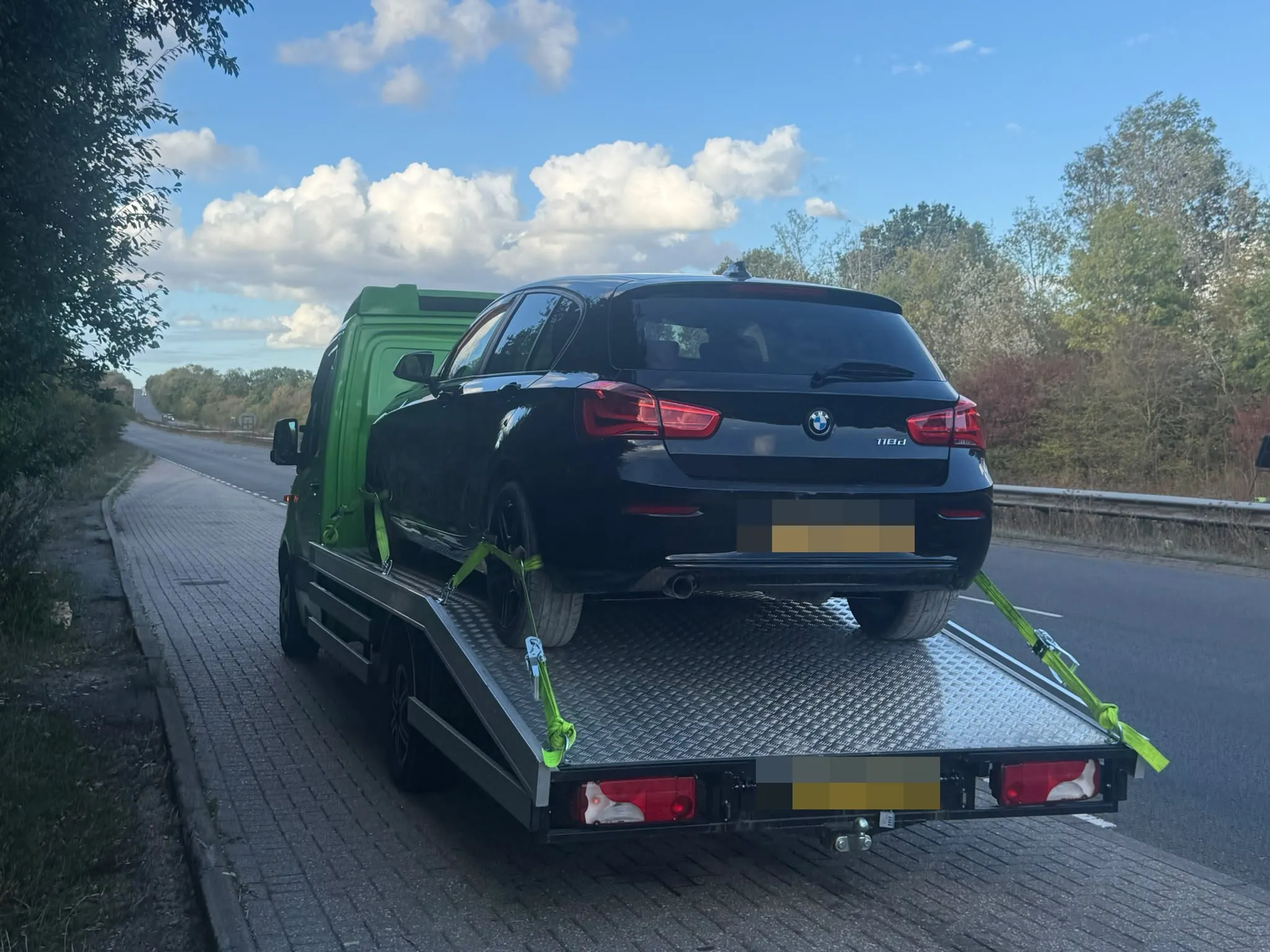 A black BMW strapped down on Toma Recovery's flatbed at the side of a dual carriageway