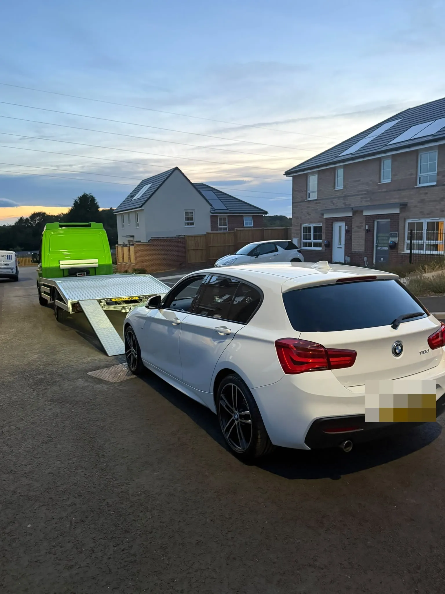 White BMW parked behind the flatbed with its ramp down near new houses