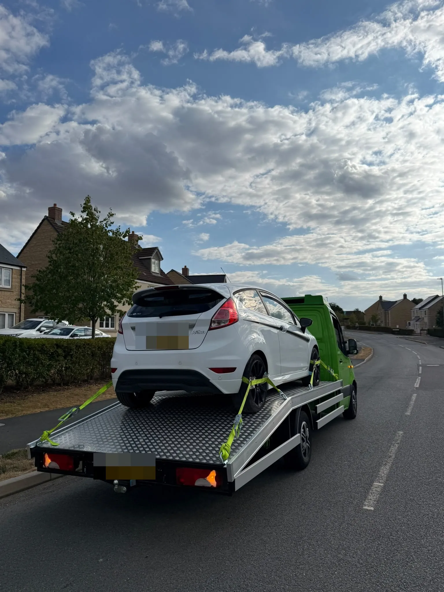 White Ford Fiesta strapped on the flatbed on a village road