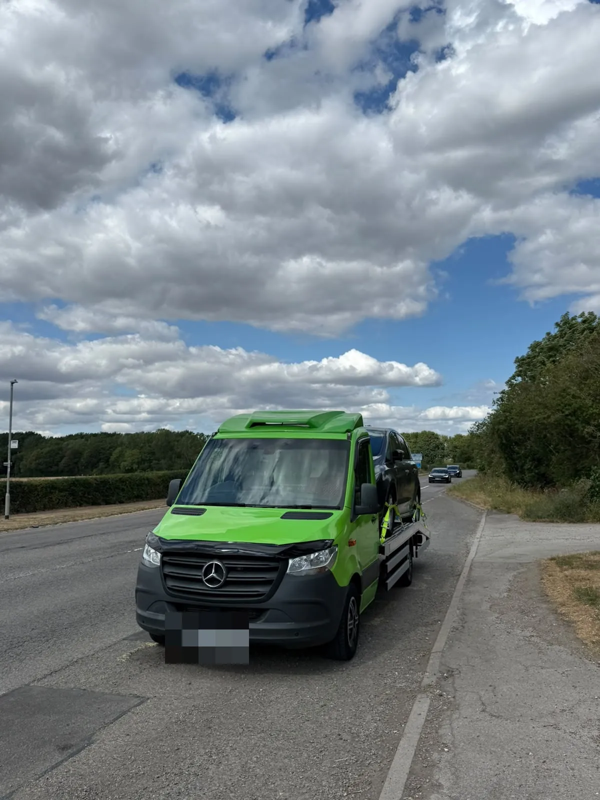 The lime green flatbed driving along a country road with a car on board