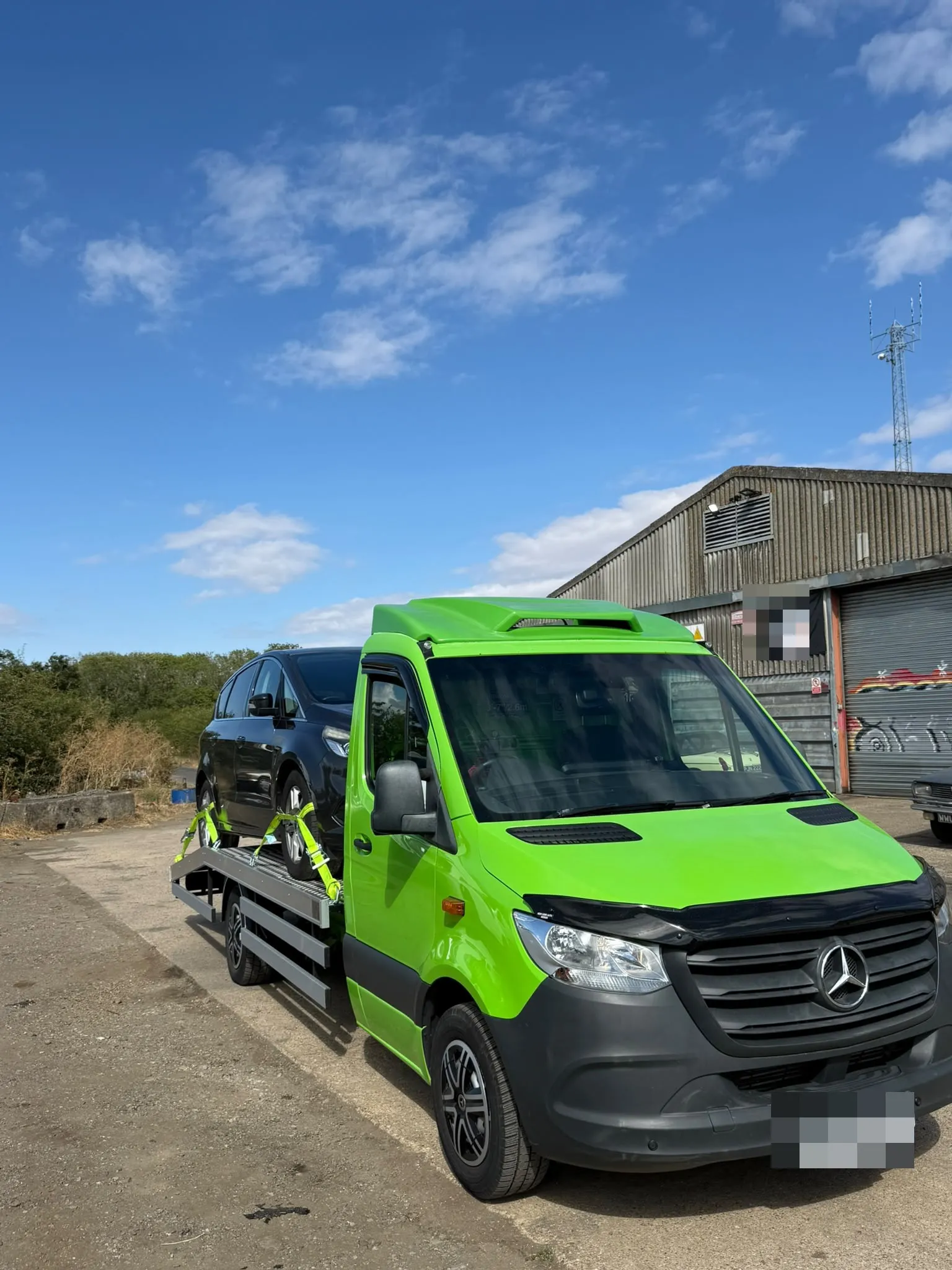 The Sprinter flatbed with a dark car on board outside an industrial unit